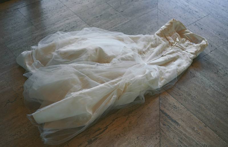 Rumpled ivory wedding dress with beaded lace and tulle lying on a stone floor