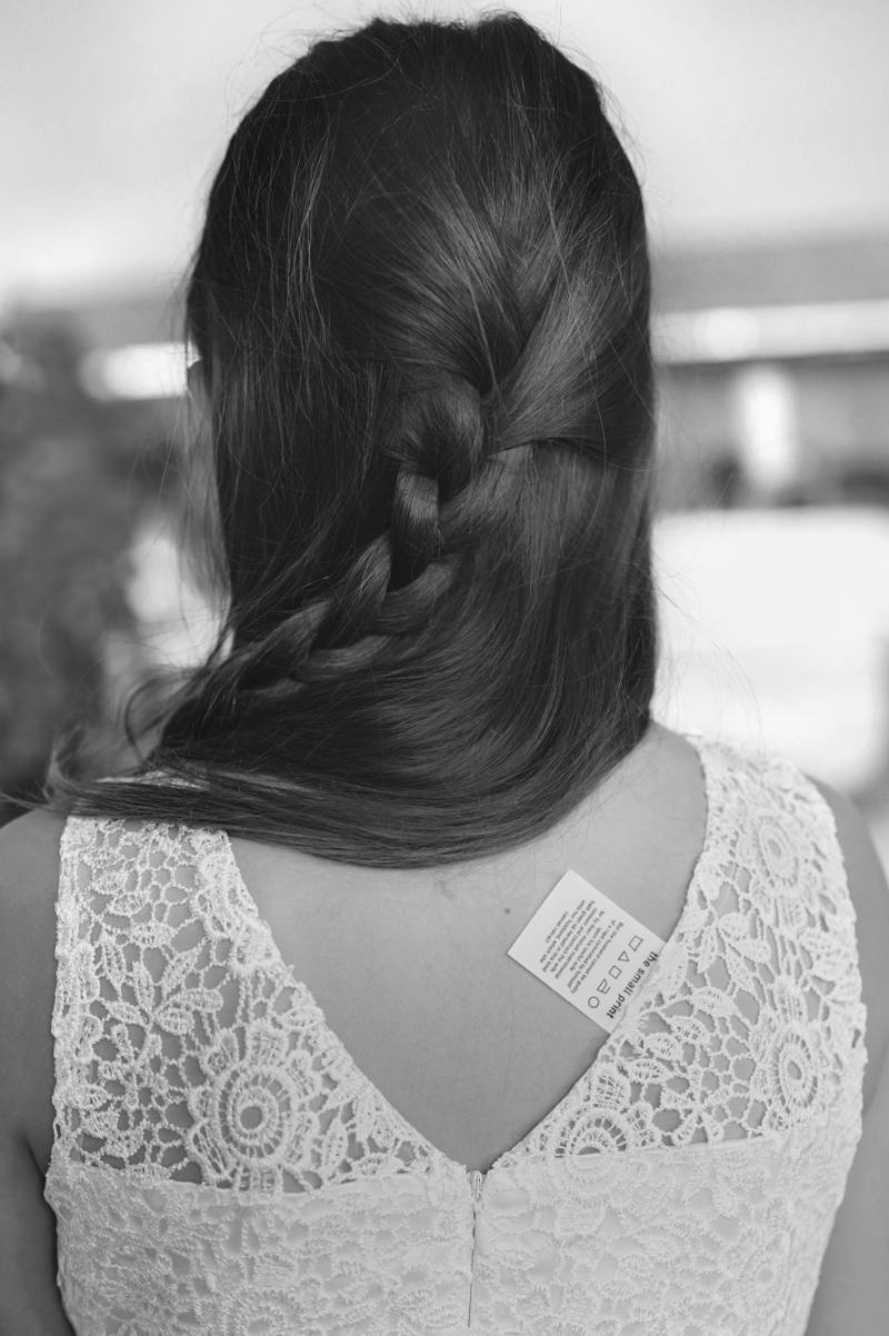 Getting ready: bride from behind, a care label tucked into the neckline of her dress
