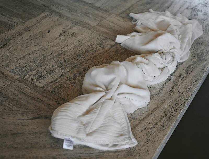 Wedding dress bound with cable ties, folded into knotted sections on a stone floor