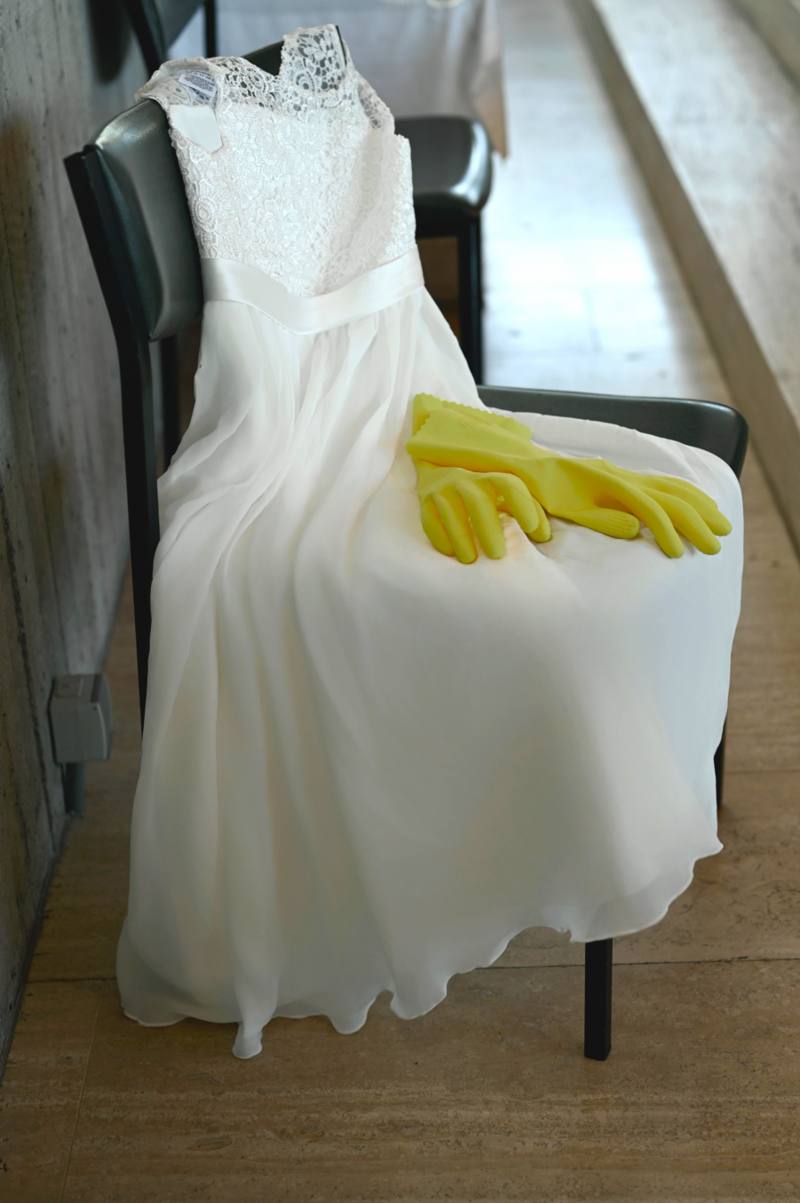 Wedding dress draped over a chair with yellow rubber household gloves resting on the seat