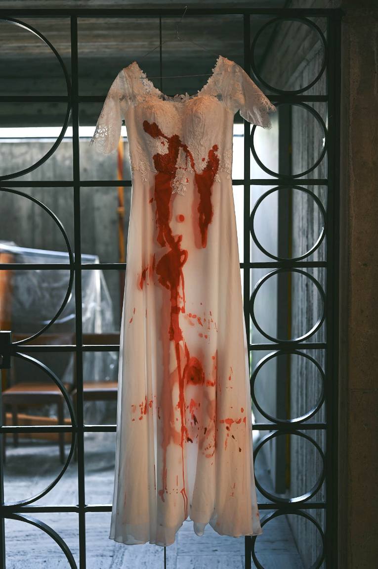Blood-stained empty wedding dress hanging on a metal grate