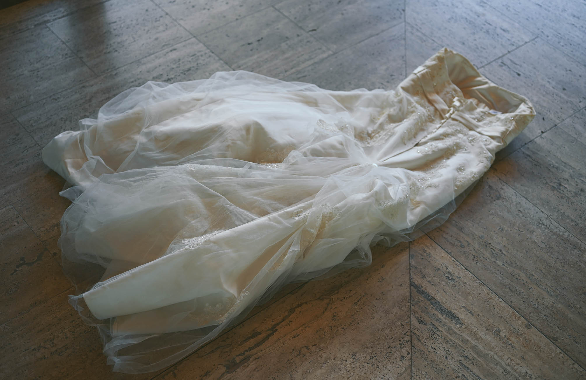 Rumpled ivory wedding dress with beaded lace and tulle lying on a stone floor