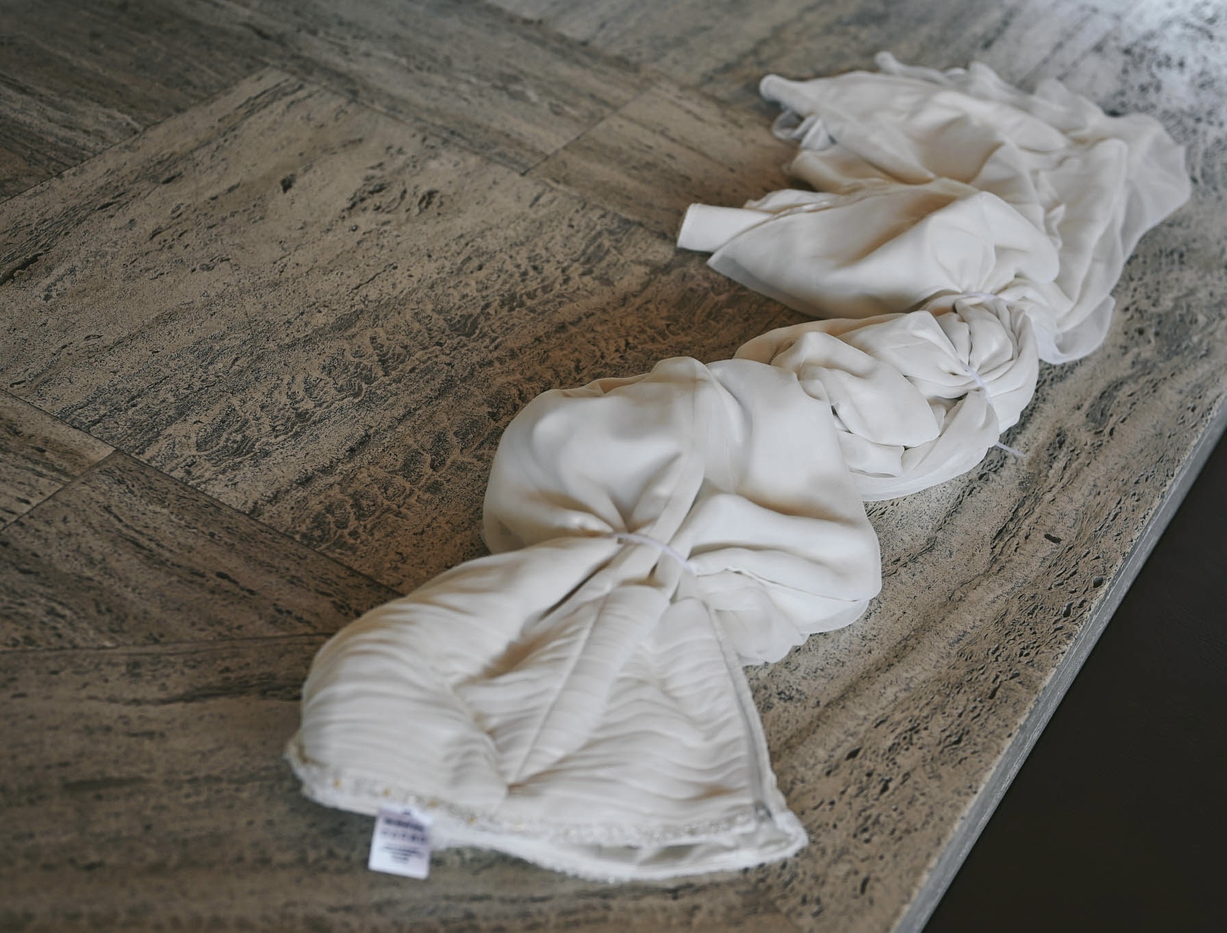 Wedding dress bound with cable ties, folded into knotted sections on a stone floor